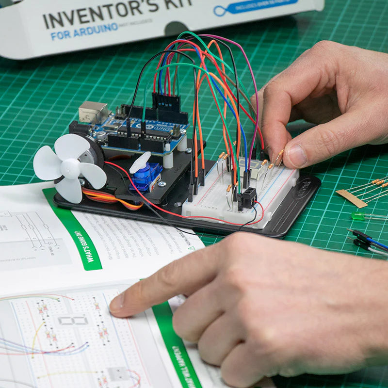 Person working with electronic components on a green cutting mat, using an 'Inventor's Kit' for Arduino.