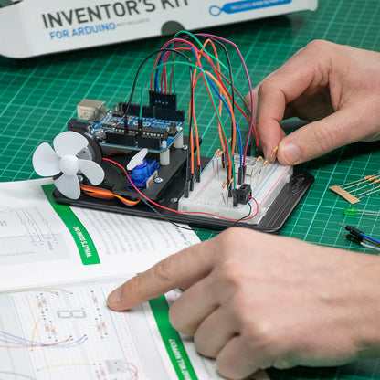 Person working with electronic components on a green cutting mat, using an 'Inventor's Kit' for Arduino.