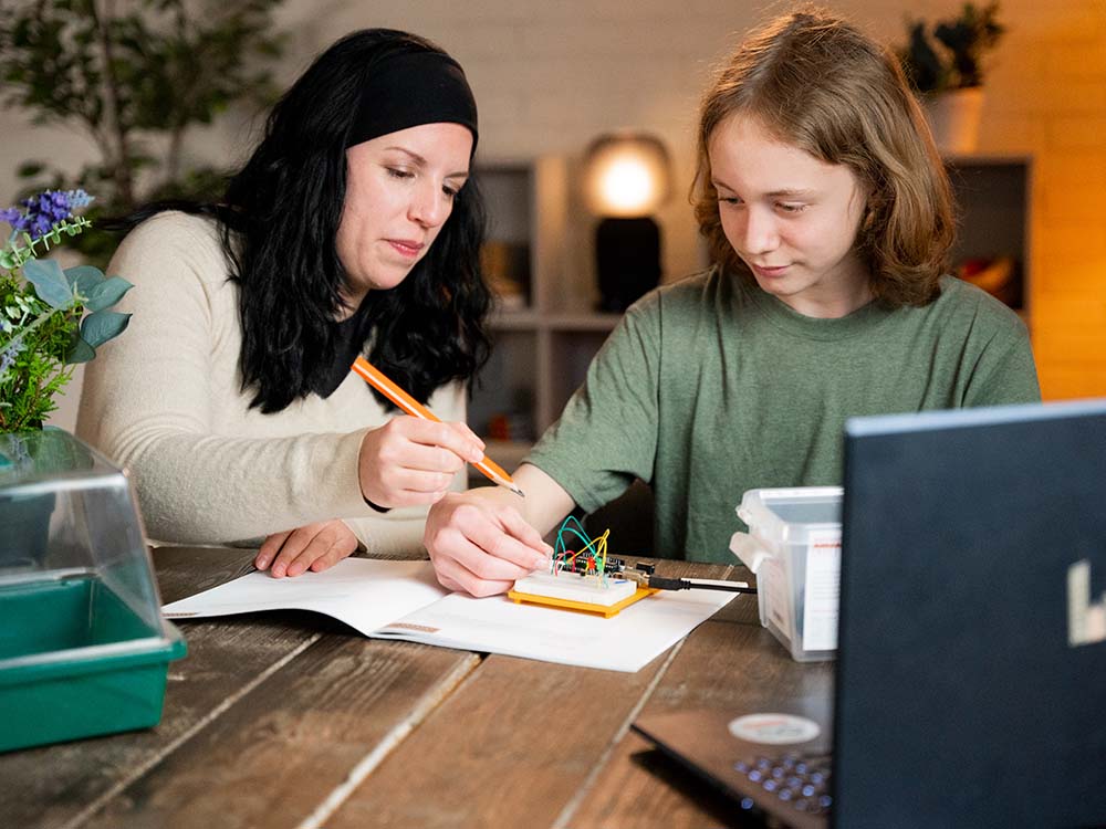 Two people working on a project at a table with a laptop and papers.